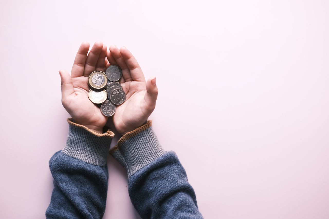 Crafting Captivating Headlines: Your awesome post title goes here Close-up of hands in sweater holding various coins, indicating savings and finance on a white background.