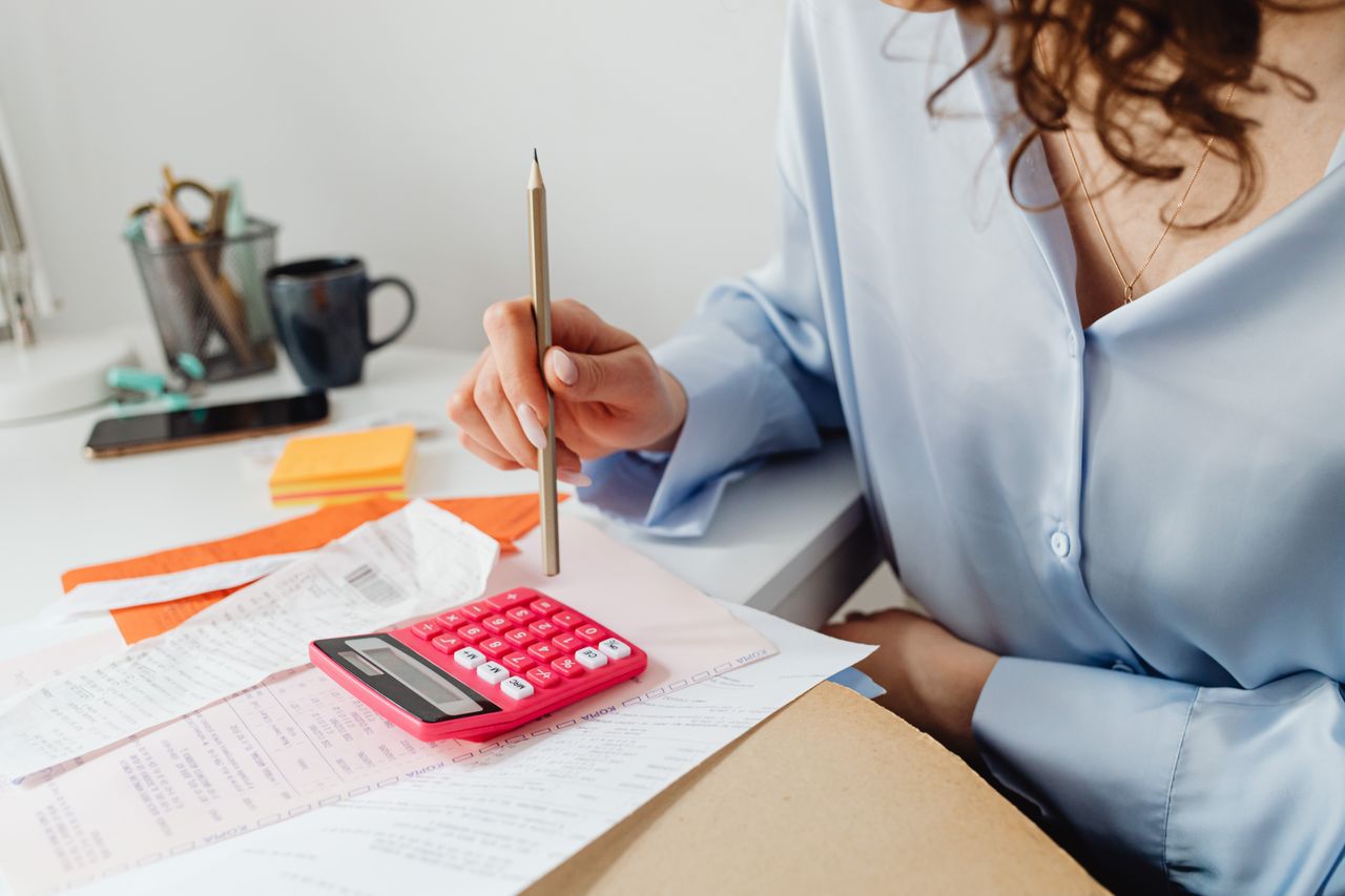 The Art of Drawing Readers In: Your attractive post title goes here A woman is calculating expenses using a calculator and papers at her desk.